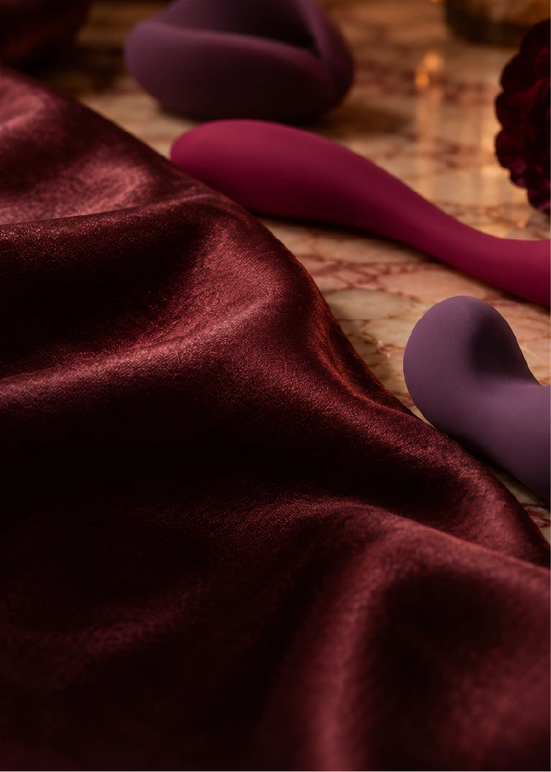 Pleasure products in plum and berry tones resting next to wine satin