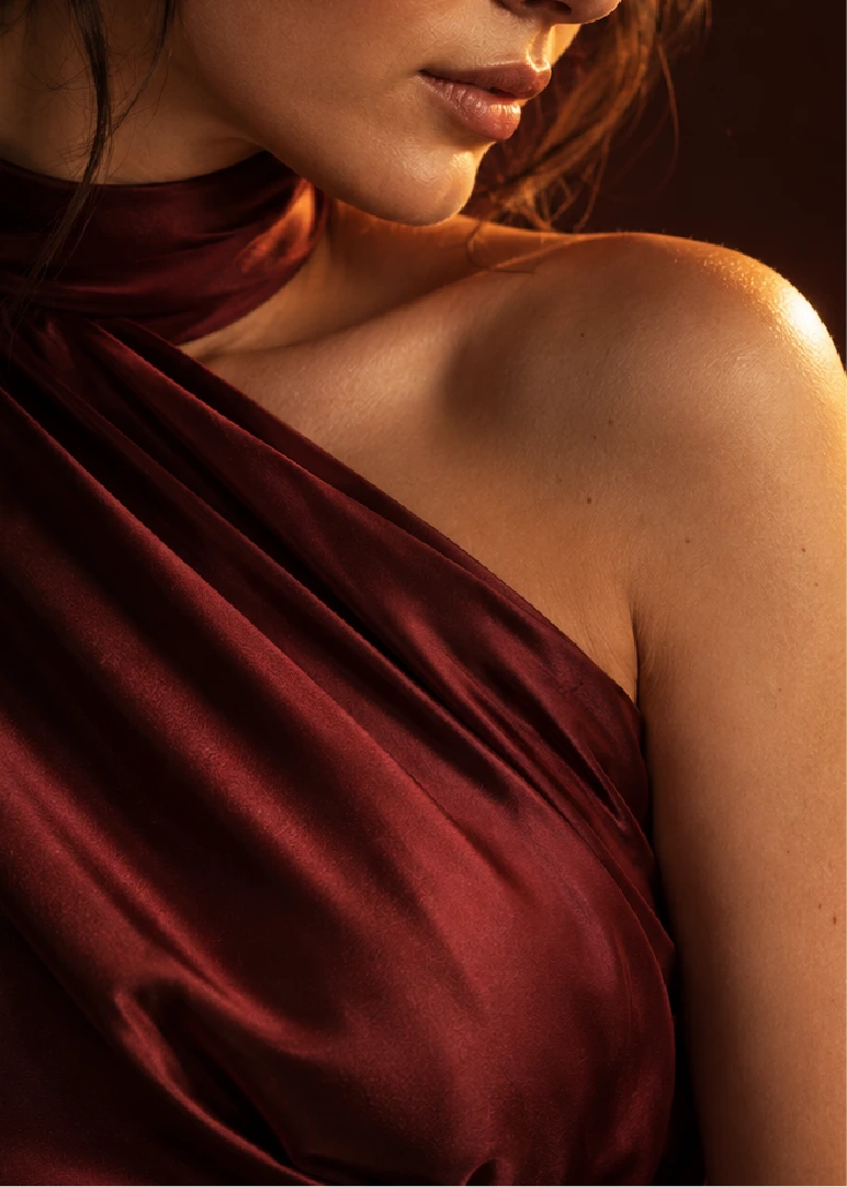 Woman in a wine satin halter top, shoulder in warm light